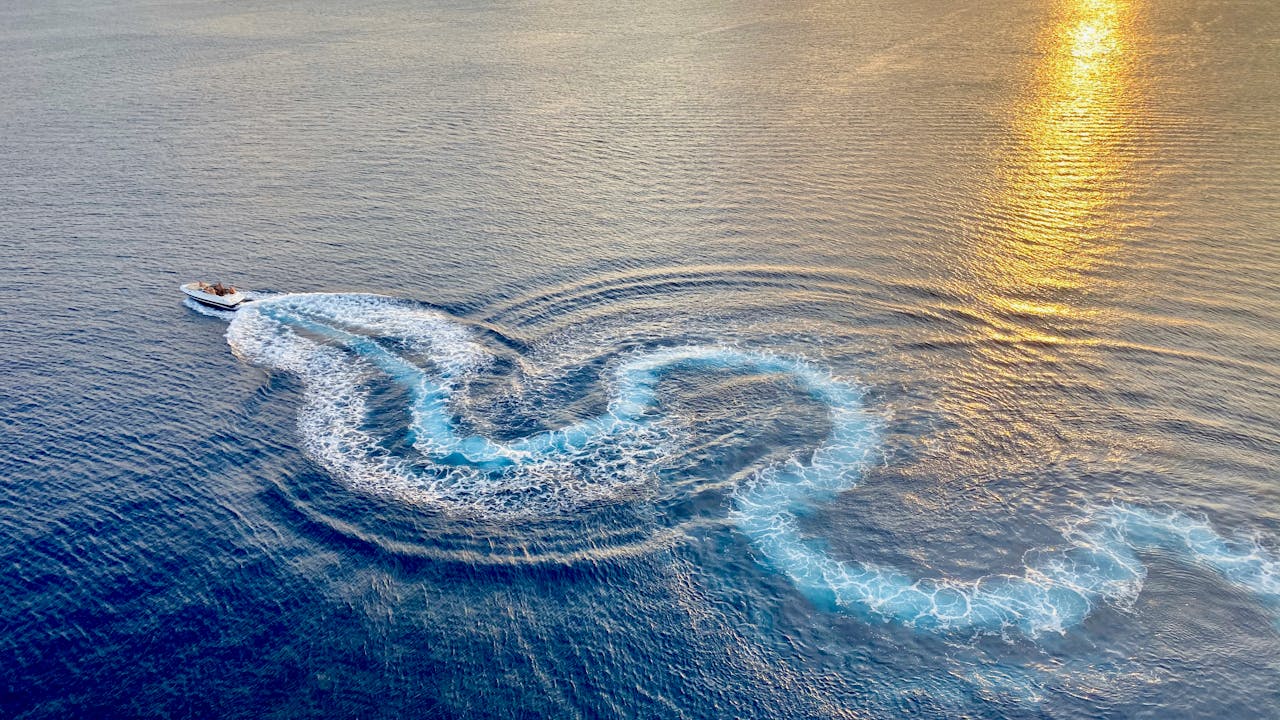 Drone shot of a speedboat making dynamic trails in the Caribbean Sea during a tranquil sunset.